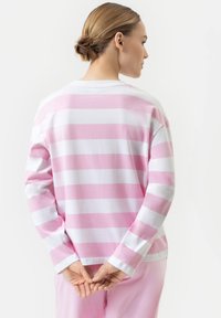 Langsleeve overhemd met horizontale roze en witte strepen, gemaakt van katoen, relaxed fit, zichtbare stiksels, gedragen met handen samengevouwen op de rug.