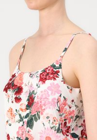 Floral print sleeveless top featuring a white background, vibrant pink and red flowers, delicate straps, and a soft textured fabric.