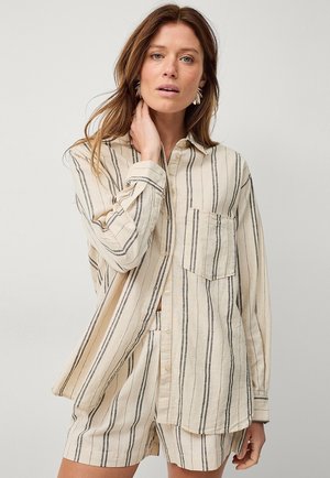 Chemise boutonnée et shorts assortis en coton beige clair avec des rayures verticales noires. Dotée d'une poche poitrine et des manches retroussées.