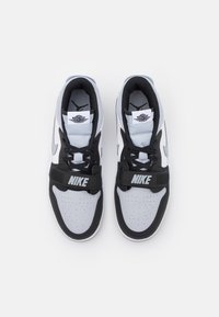 Černobílé tenisky se syntetickým svrškem, perforovanou špičkou, nastavitelným popruhem a výrazným logem Nike na popruhu a jazyku.