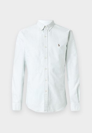 Chemise à manches longues rayée bleu clair et blanche avec un col boutonné et une patte de boutonnage à l'avant, arborant un petit logo brodé.