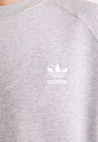 Felpa grigia in morbido tessuto, con un logo Adidas ricamato in bianco che presenta tre strisce e un design a trifoglio sul petto.
