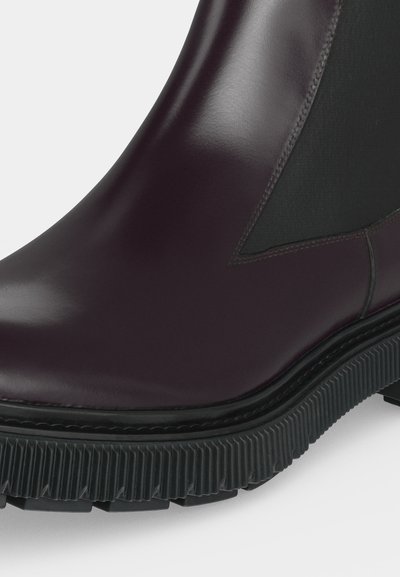 Gros plan d'une botte en cuir sombre poli avec un panneau latéral élastique noir et une semelle épaisse en caoutchouc noir rainurée.