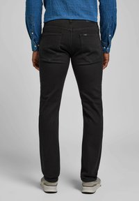 Jeans de mezclilla negra con un ajuste slim, que cuentan con dos bolsillos traseros, costuras sutiles y combinados con zapatillas gris claro.
