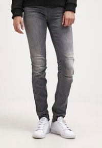 Šedé denimové džíny s úzkým střihem, se švy na kolenou a mírně vybledlou texturou, spárované s bílými sportovními botami.