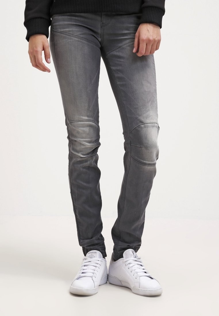 Šedé denimové džíny s úzkým střihem, se švy na kolenou a mírně vybledlou texturou, spárované s bílými sportovními botami.