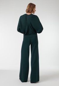 Donkergroene, geribde trui met oversized mouwen en een fitted tailleband, gecombineerd met wijde broekspijpen, wat een vloeiende silhouet creëert.