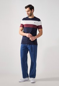 Navy and white striped t-shirt with maroon accents, cotton material, short sleeves; paired with blue denim jeans and white sneakers.