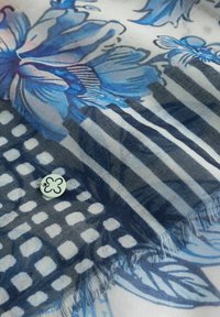 Blauer Stoff mit Blumenmuster und Streifen, versehen mit einem kleinen weißen runden Etikett mit einem schwarzen vierblättrigen Kleeblatt-Motiv.