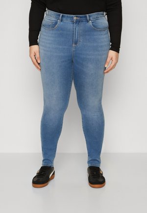 Blue denim skinny jeans with a high waist, five pockets, and subtle fading details, paired with black sneakers featuring brown soles.