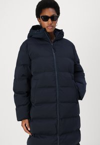 Navy puffer coat with a zip front, hood, and large quilted panels. Features side pockets and a high collar for extra warmth.