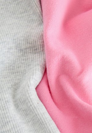 Tissu en mélange de coton gris et rose, offrant une texture lisse avec un motif à côtes sur le côté gris et une finition douce sur le côté rose.