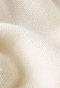 Vitt stickat tyg med en mjuk textur och synligt sömnads mönster, som har en lätt luddig yta och neutral ton.