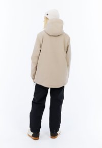 Beige wasserdichte Jacke mit Kapuze, schwarze Hosen und beige-schwarze Schuhe. Verfügt über eine lockere Passform und elastische Bündchen.