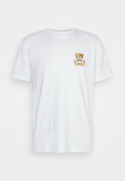 Camiseta de algodón blanca con un oso de peluche bordado y una etiqueta que dice "Moschino" en la parte izquierda del pecho. Mangas cortas, escote redondo.