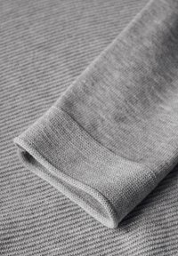 Harmaa neulepusero, jossa on teksturoitu pinta, käännetyt hihat ja sileä viimeistely. Kangas esittää hienoa, tasaisesti toistuvaa kuviointia.