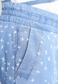 Helle blaue Shorts aus weichem Material, mit einem weißen Vogelmuster, elastischem Bund und einem kleinen "RAW"-Logo an der Seite.