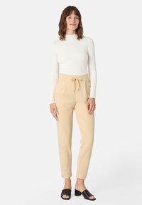 Beige kalhoty s elastickým pasem, s bočními kapsami. V kombinaci s bílým přiléhavým topem s dlouhým rukávem a černými otevřenými block heels.