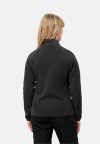 Giacca in pile nera con collo alto, maniche raglan e zip laterali. Caratterizzata da una texture liscia e un design aderente.