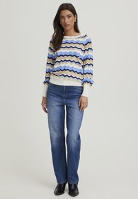 Pull en tricot avec un motif en zigzag bleu, beige et noir, associé à un jean droit bleu clair et des bottines noires.