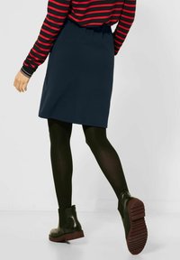 Marinblå kjol med resår i midjan, kombinerad med svarta strumpbyxor och svarta stövlar i ankellängd med texturerad sula. Randig topp synlig.