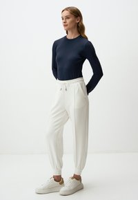 Marineblaues Langarmoberteil mit strukturierten Ärmeln, kombiniert mit weißen, schmal zulaufenden Hosen mit elastischem Bund und Taschen. Cremefarbene Sneakers runden den Look ab.