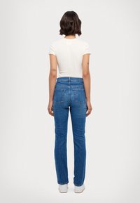 Bílý texturovaný top s krátkými vroubkovanými rukávy, spárovaný s vysokým modrým denimem, který má klasický střih a zadní kapsy.