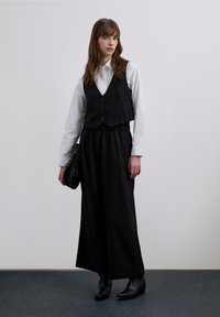 Czarna kamizelka w prążki noszona na białej koszuli zapinanej na guziki, zestawiona z czarnymi szerokimi spodniami i botkami za kostkę. Dopełnieniem stroju jest czarna torebka.