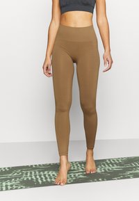Leggings marroni a vita alta realizzati in tessuto elasticizzato, con silhouette aderente, caratterizzati da un sottile dettaglio in rete lungo i fianchi.