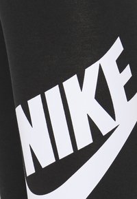 Leggings sportivi neri con un grande logo bianco "Nike" e il design dello swoosh lungo il lato, realizzati in un materiale liscio e elasticizzato.