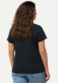 Zwarte T-shirt met korte mouwen en een ronde hals. Gemaakt van zachte stof. Eenvoudig ontwerp met een rechte zoom. Zittend model met krullend haar.