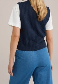 Laikattu meriväri-vuoriväri on kuvioitu design ja se on käytetty valkoisen t-paidan päällä. Epämuodolliset siniset farkut täydentävät asusteet.