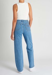 Vaaleansininen farkkukangas, leveälahkeiset farkut, joissa on korkea vyötärö ja kaksi takataskua. Farkuissa on vaalea logo-ompelu oikean taskun lähell ä.