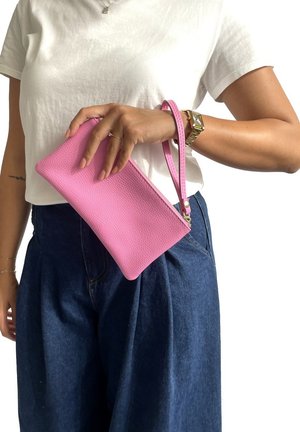 Clutch in pelle rosa texturizzata con un cinturino da polso, tenuto in mano. Presenta una chiusura con zip e un design rettangolare slim, posizionato su uno sfondo bianco semplice.
