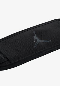 Pulsera negra de tela con acabado texturizado, que presenta un logotipo de Jordan negro brillante y un cierre seguro. Diseño compacto y ergonómico.