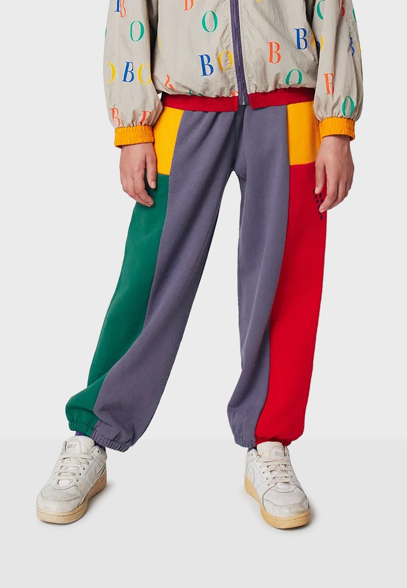 Kolorowe dresy z patchworkowym wzorem w odcieniach szarości, czerwieni, zieleni i żółci, z elastycznymi mankietami, w połączeniu z białymi sneakersami.