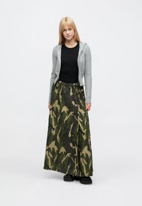 Maxiseelik rohelises kamuflaažkangas, kõrge vöökohaga, külgmiste pandlate ja lõdva lõikega. Kombineeritud halli kardiganiga musta pluusi kohal.