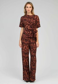 Combinaison imprimée avec un motif noir et orange, manches courtes, taille cintrée, et pantalons larges en tissu lisse.