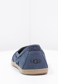 Marineblauwe instapschoen met een gestructureerde stof bovenkant, jute-stijl zool en UGG-branding. Kenmerkt zich door gestikte details en een ronde neusdesign.