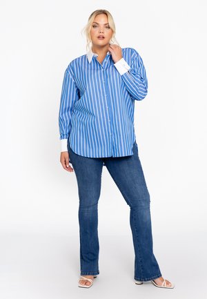 Blauw-wit gestreepte button-up shirt met een witte kraag, gecombineerd met uitlopende blauwe jeans en witte sandalen. Soepele stof, lange mouwen.