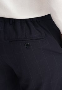 Marineblauwe geruite broek met een relaxte pasvorm, voorzien van een enkele achterzak en een knoopsluiting. Zachte stof met een subtiele textuur.