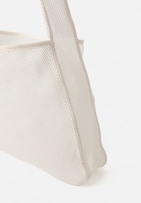 Sac en maille blanche avec une forme structurée, présentant un tissu texturé et des coutures renforcées sur les bords. Design simple, construction légère.