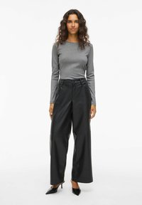 Maglietta grigia a maniche lunghe abbinata a pantaloni ampi in pelle nera a vita alta. L'outfit presenta texture lisce e una vestibilità morbida.