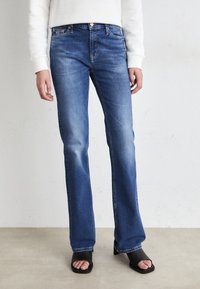 Blue straight-leg jeans made of denim, featuring a five-pocket design and subtle fading. Paired with black open-toed heeled sandals.