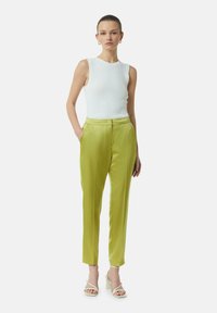 Zielone satynowe spodnie o gładkiej fakturze, z bocznymi kieszeniami i dopasowanym krojem. Połączone z białym, żebrowanym topem bez rękawów i sandałami.