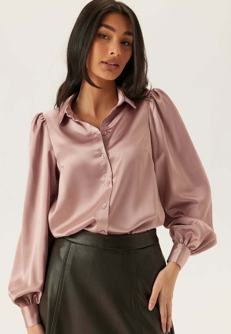 Blouse en satin mauve avec fermeture à boutons sur le devant, manches bouffantes et coupe décontractée, associée à une jupe en cuir noire.