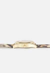 Reloj en tono dorado con una esfera redonda y una correa de ante con estampado de leopardo. Cuenta con una corona texturizada y un cristal transparente en la esfera.