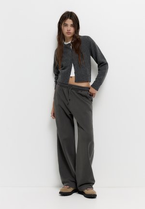 Šedý pletený kardigan přes bílý crop top, doplněný volnými šedými tepláky. Oblečení má uvolněný střih a elastický pas.