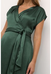 Groene wikkeljurk van textuurstof. Heeft een v-halslijn, korte mouwen en een tailleband, wat een vloeiende silhoutte creëert.