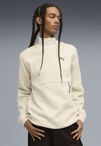 Felpa beige chiaro con colletto alto, logo nero sul petto e tasca con zip. Realizzata in tessuto morbido con vestibilità comoda.